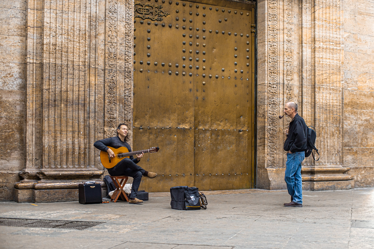 Músico callejero tocando guitarra frente a una puerta dorada en un entorno urbano, fotografía de autor de Fabián Borelli.